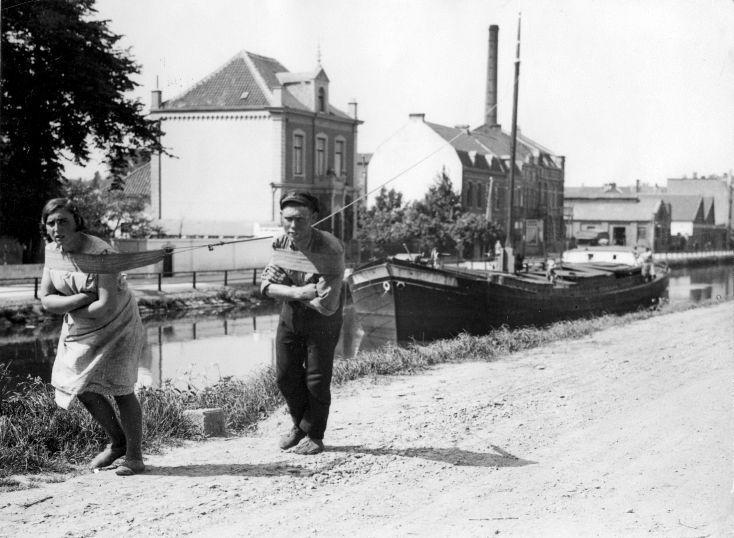Een man en een vrouw trekken samen een trekschuit door een binnenkanaal. Plaats onbekend, 27 mei 1931.